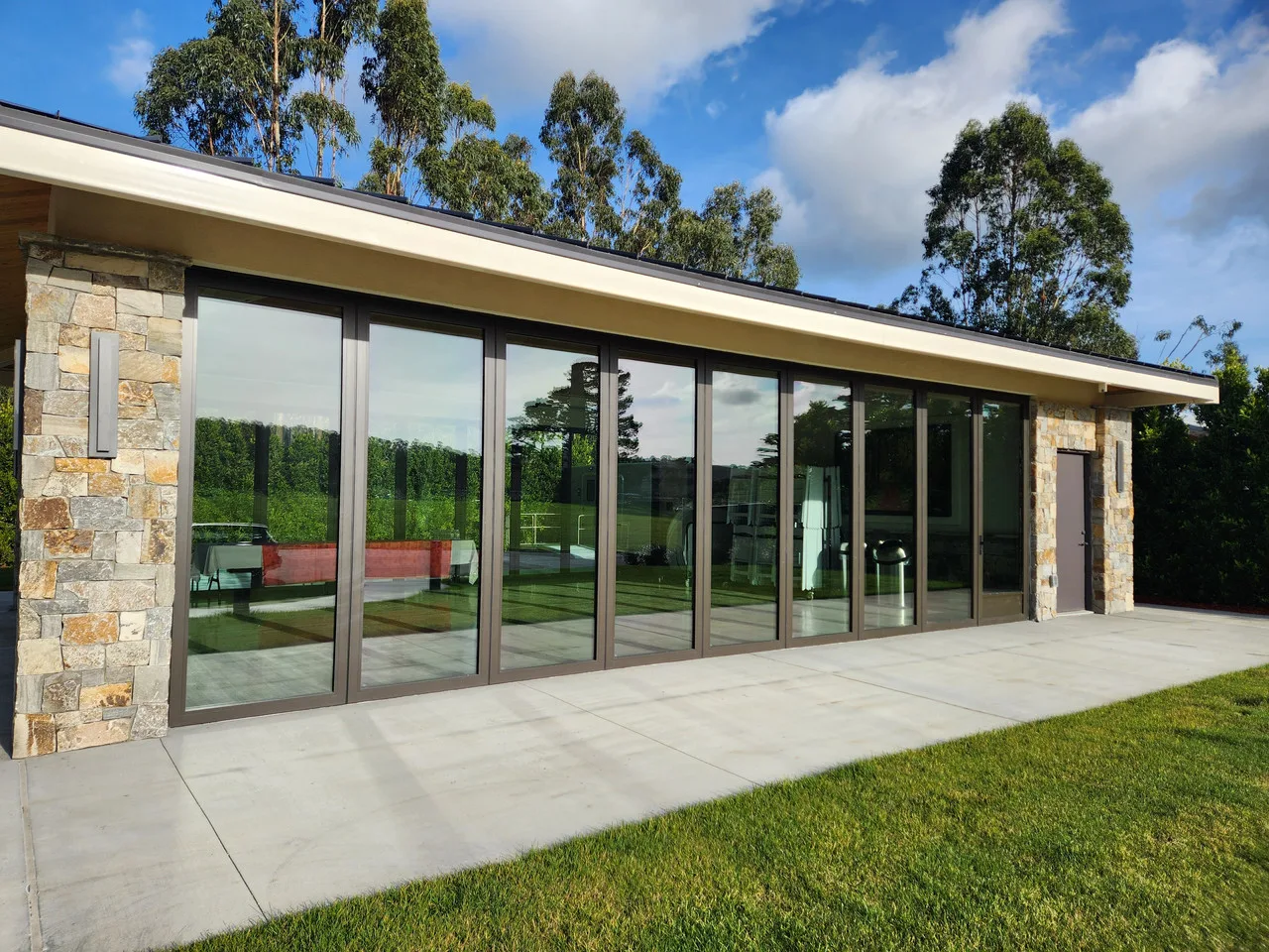Expansive dark-framed glass panels between stone columns overlooking a patio and lawn